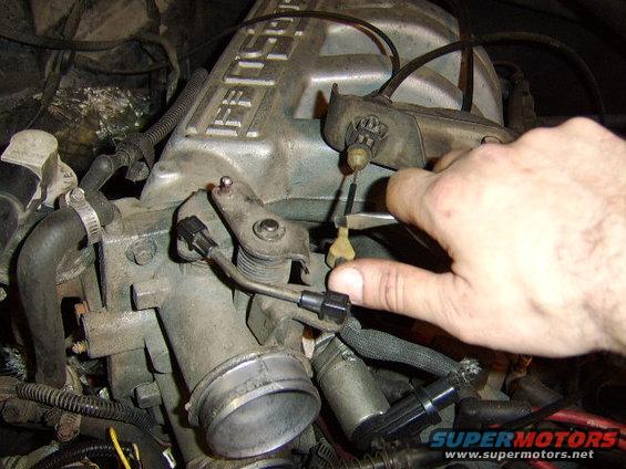 change-oil-pan-gasket-and-valve-cover-gasket-010.jpg the tranny cable is removed by pulling towards yourself and lifting up. 
At the bracket towards the rear, use a pair of pliers to squeese the retaining clips together, thus allowing you to push the cable through.